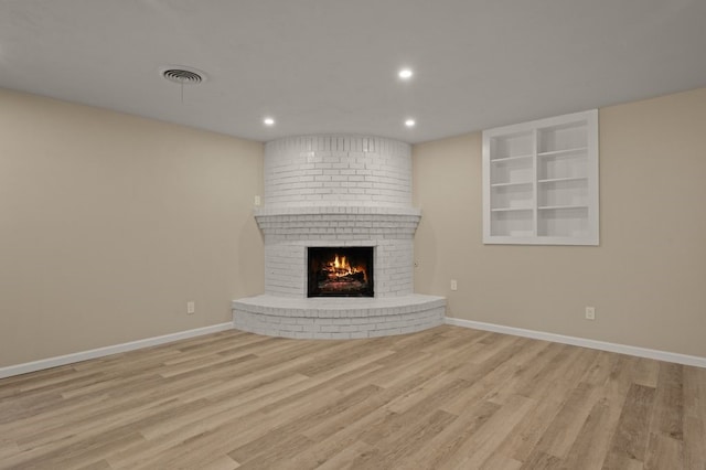 unfurnished living room with light wood-type flooring and a brick fireplace