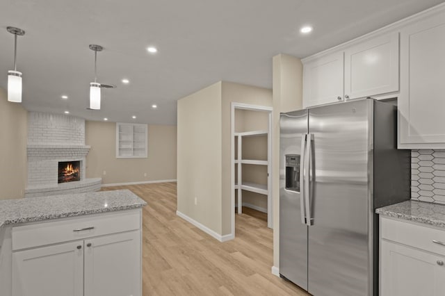 kitchen featuring stainless steel fridge, light hardwood / wood-style flooring, backsplash, a brick fireplace, and white cabinetry