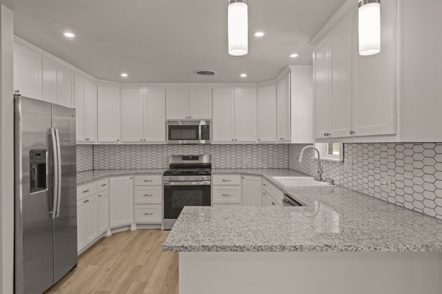 kitchen featuring decorative light fixtures, appliances with stainless steel finishes, white cabinetry, and light hardwood / wood-style floors