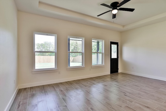 empty room featuring a raised ceiling, ceiling fan, and light hardwood / wood-style floors