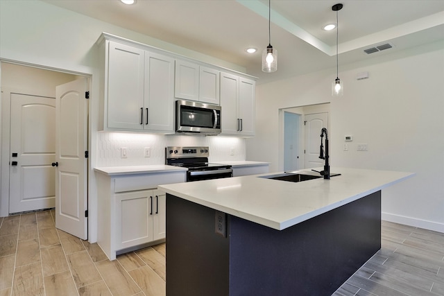 kitchen featuring hanging light fixtures, stainless steel appliances, white cabinetry, and a kitchen island with sink