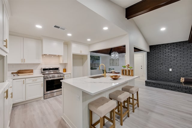 kitchen with white cabinets, a kitchen breakfast bar, sink, and stainless steel range