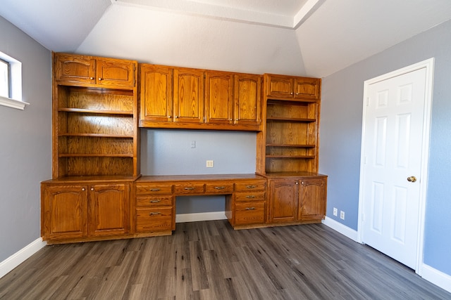 unfurnished office featuring lofted ceiling, built in desk, and dark hardwood / wood-style flooring