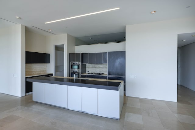 kitchen featuring tasteful backsplash, appliances with stainless steel finishes, light tile patterned floors, and an island with sink