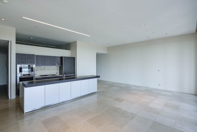 kitchen featuring appliances with stainless steel finishes, light tile patterned floors, an island with sink, and decorative backsplash