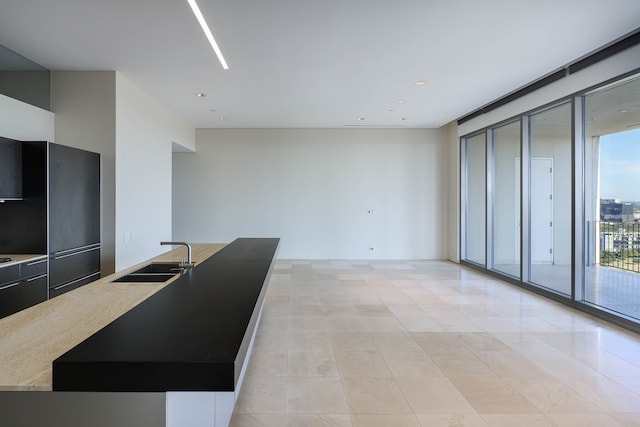 kitchen with light tile patterned flooring, a wall of windows, sink, and a center island with sink