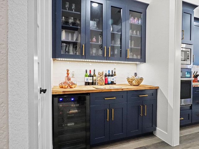 bar with light wood-type flooring, wood counters, beverage cooler, appliances with stainless steel finishes, and blue cabinetry