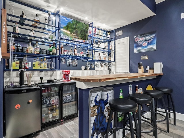 bar with wood-type flooring, refrigerator, and beverage cooler