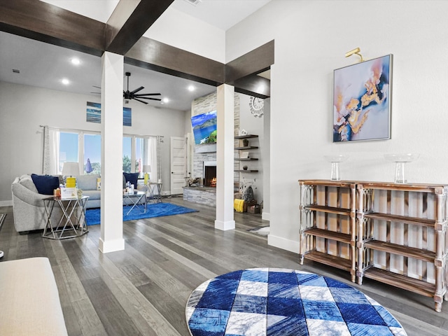 interior space featuring ceiling fan, a stone fireplace, beamed ceiling, and dark hardwood / wood-style floors