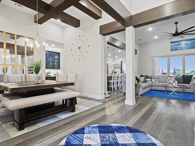 dining space with a towering ceiling, ceiling fan with notable chandelier, dark hardwood / wood-style floors, and beam ceiling