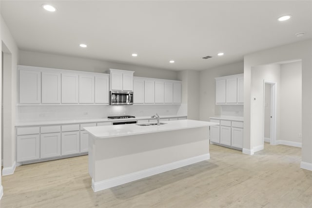 kitchen with light hardwood / wood-style floors, a kitchen island with sink, sink, stainless steel appliances, and white cabinetry