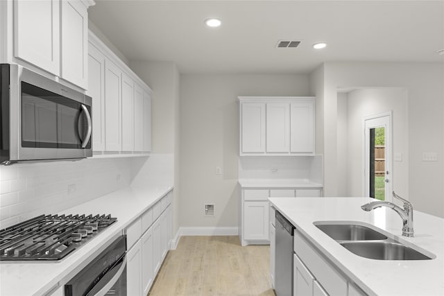 kitchen with white cabinets, sink, backsplash, appliances with stainless steel finishes, and light wood-type flooring