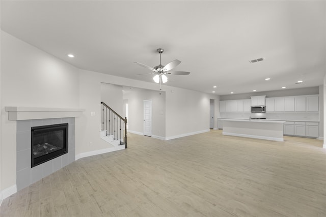 unfurnished living room with ceiling fan, a tiled fireplace, and light hardwood / wood-style floors