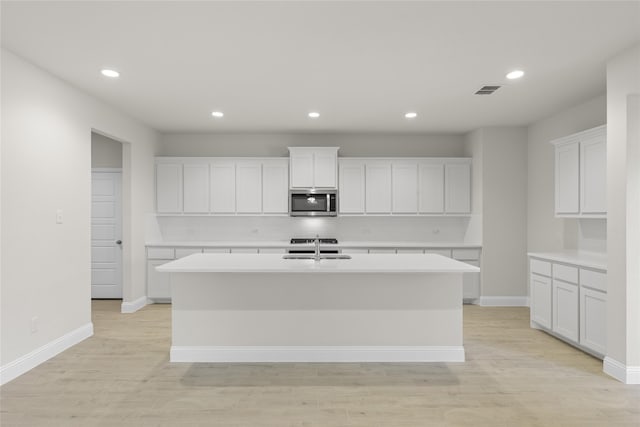 kitchen with white cabinets, a center island with sink, light hardwood / wood-style flooring, and sink