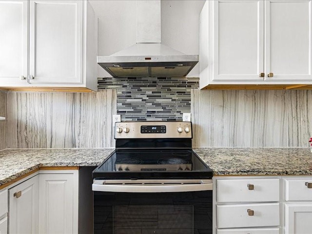 kitchen featuring wall chimney range hood, backsplash, light stone countertops, white cabinets, and stainless steel electric stove