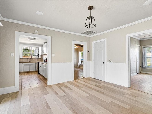 unfurnished dining area featuring ornamental molding, a textured ceiling, and light hardwood / wood-style flooring