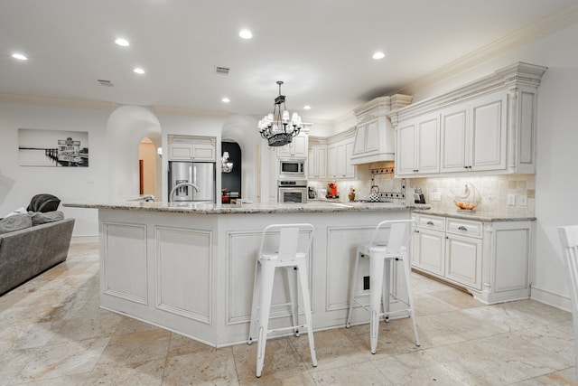 kitchen featuring a large island with sink, stainless steel appliances, white cabinets, pendant lighting, and a breakfast bar area