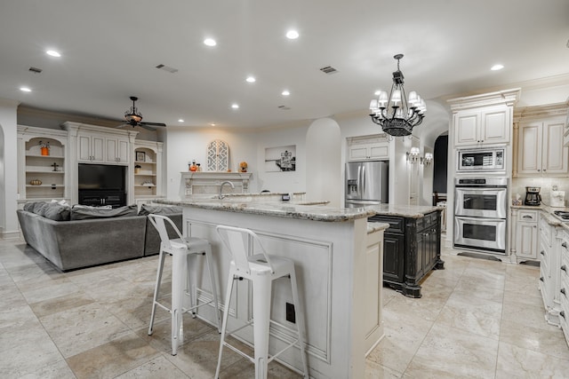 kitchen with light stone counters, pendant lighting, a large island, stainless steel appliances, and ceiling fan with notable chandelier