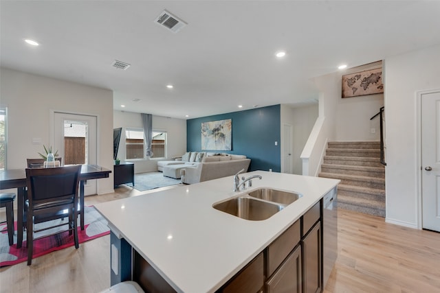 kitchen with light hardwood / wood-style flooring, stainless steel dishwasher, sink, and a kitchen island with sink