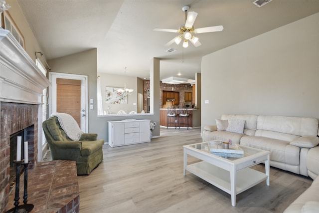 living room with a fireplace, ceiling fan with notable chandelier, light hardwood / wood-style floors, and vaulted ceiling