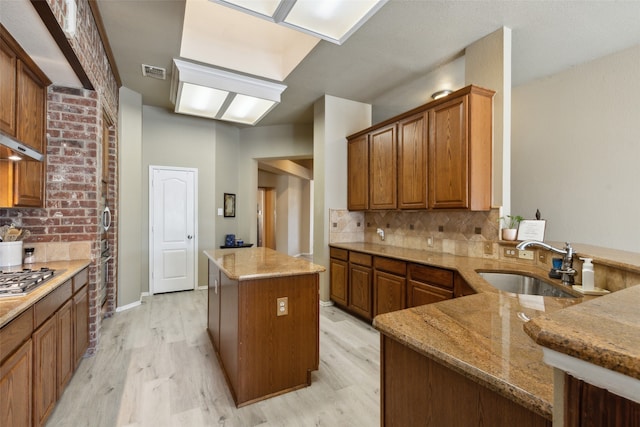 kitchen featuring light stone countertops, a center island, sink, kitchen peninsula, and light hardwood / wood-style floors