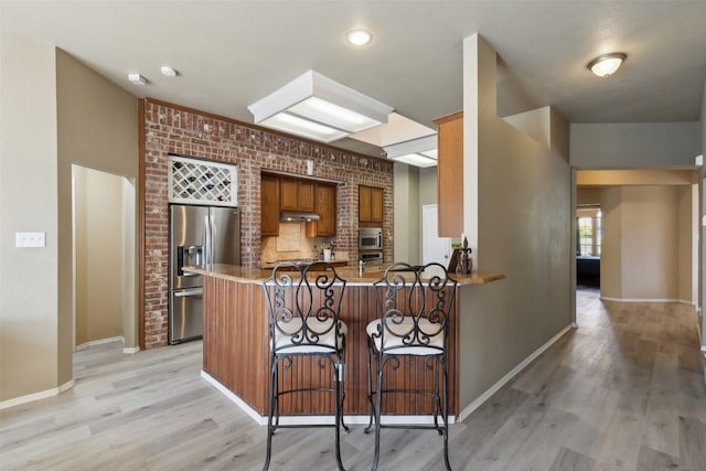 kitchen with a kitchen breakfast bar, kitchen peninsula, appliances with stainless steel finishes, and light wood-type flooring