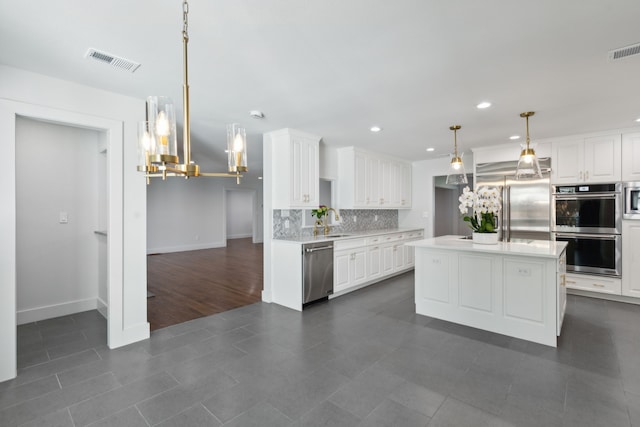 kitchen with built in appliances, a kitchen island, decorative light fixtures, decorative backsplash, and white cabinets