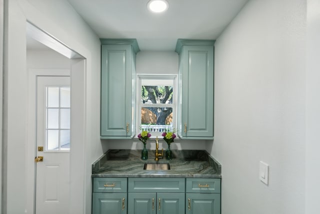 bar with dark stone countertops, green cabinets, and sink