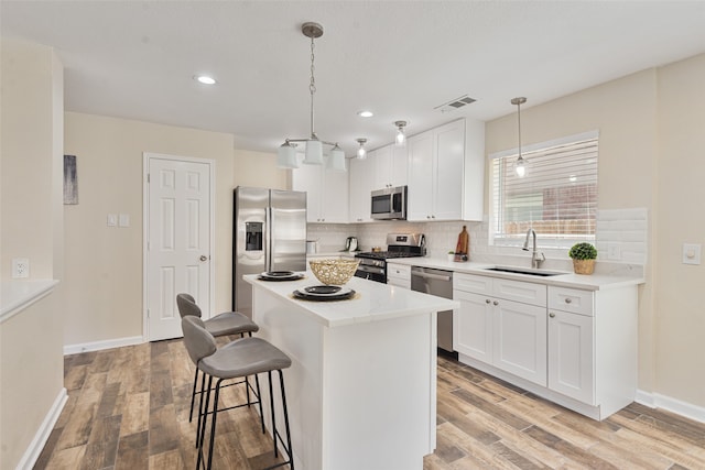 kitchen with appliances with stainless steel finishes, a center island, hanging light fixtures, sink, and white cabinets