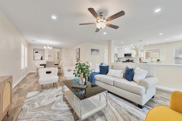 living room with ceiling fan with notable chandelier, plenty of natural light, and light hardwood / wood-style flooring