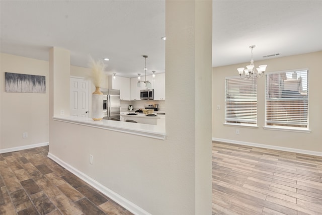 kitchen with pendant lighting, wood-type flooring, appliances with stainless steel finishes, and white cabinetry