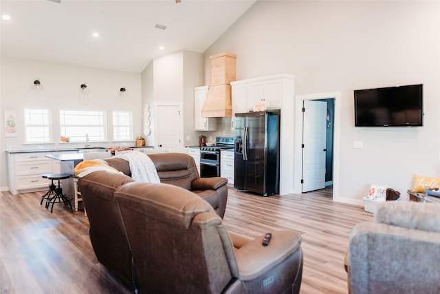 living room with sink, light hardwood / wood-style floors, and high vaulted ceiling