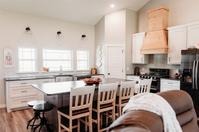 kitchen with premium range hood, sink, white cabinetry, appliances with stainless steel finishes, and vaulted ceiling