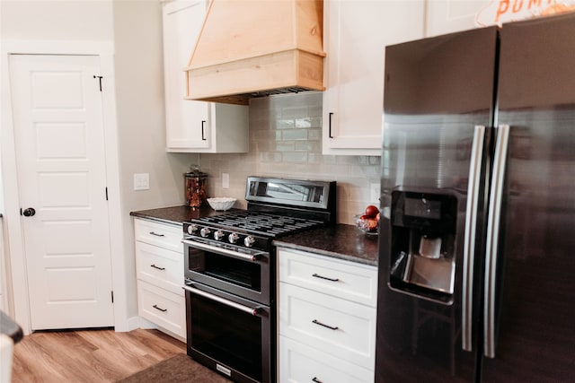 kitchen with white cabinets, premium range hood, light hardwood / wood-style flooring, appliances with stainless steel finishes, and dark stone counters