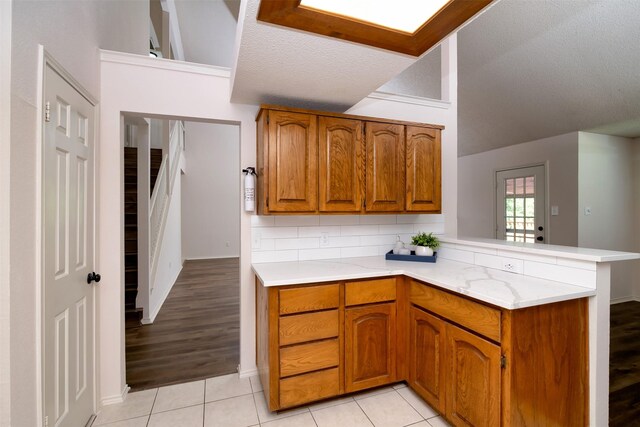 kitchen featuring a textured ceiling, kitchen peninsula, light hardwood / wood-style flooring, and tasteful backsplash