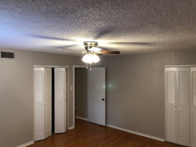 unfurnished bedroom with ceiling fan, multiple closets, a textured ceiling, and dark hardwood / wood-style floors