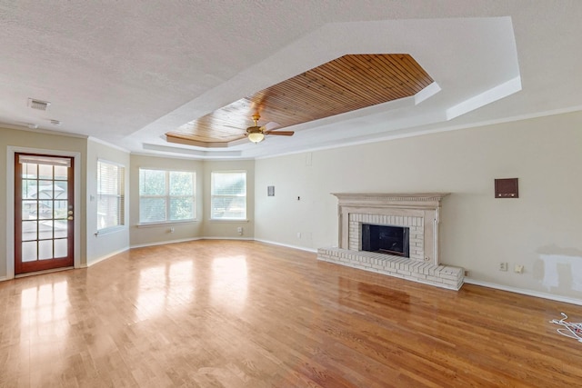 unfurnished living room featuring light wood-type flooring, a tray ceiling, ceiling fan, and a fireplace