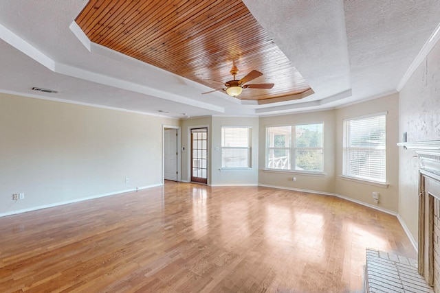 unfurnished living room featuring a textured ceiling, a tray ceiling, ceiling fan, light hardwood / wood-style flooring, and ornamental molding