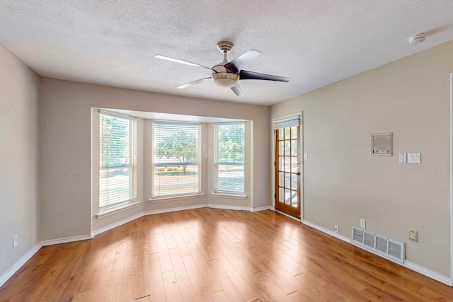 spare room with light wood-type flooring, ceiling fan, and a textured ceiling