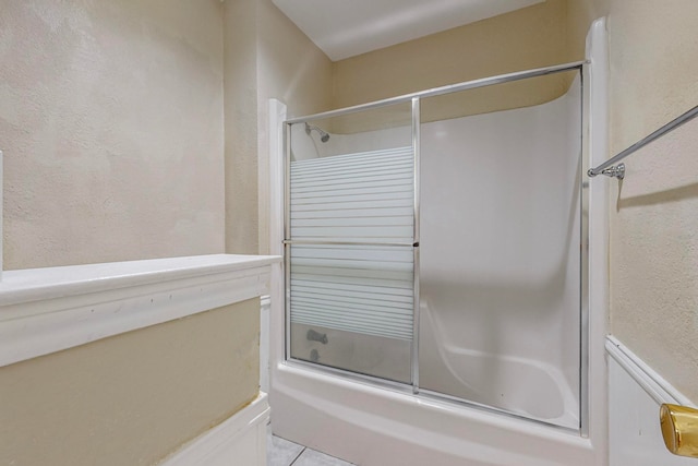 bathroom with bath / shower combo with glass door and tile patterned flooring