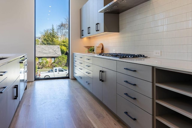 kitchen with white cabinetry, wall chimney range hood, backsplash, light wood-type flooring, and stainless steel gas stovetop