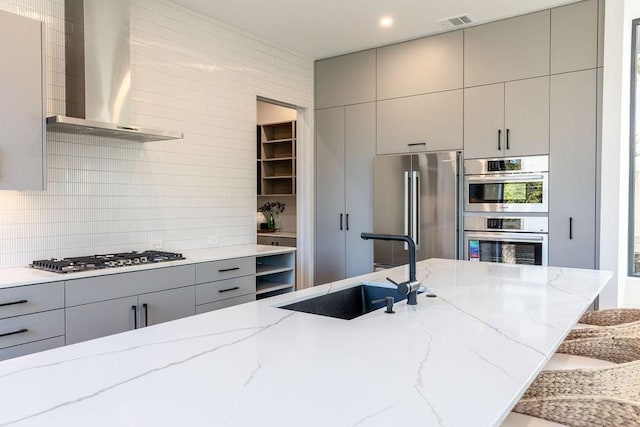 kitchen with light stone countertops, extractor fan, stainless steel appliances, sink, and gray cabinets