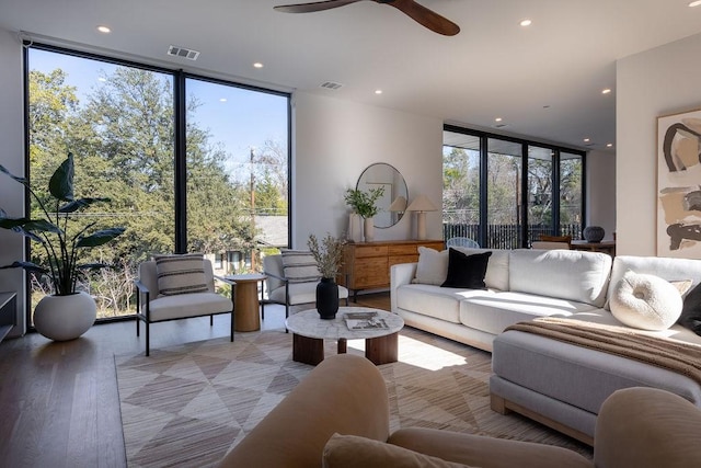 living room featuring ceiling fan, a wall of windows, light hardwood / wood-style flooring, and a healthy amount of sunlight