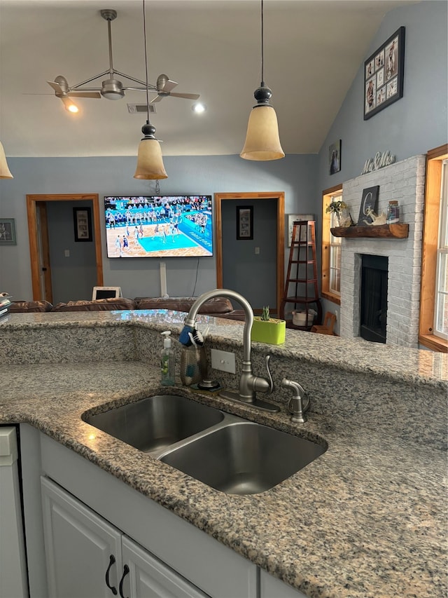 kitchen with vaulted ceiling, white cabinetry, a brick fireplace, ceiling fan, and sink