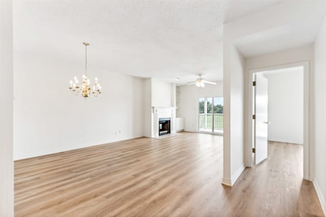 unfurnished living room featuring ceiling fan with notable chandelier, a textured ceiling, and light wood-type flooring