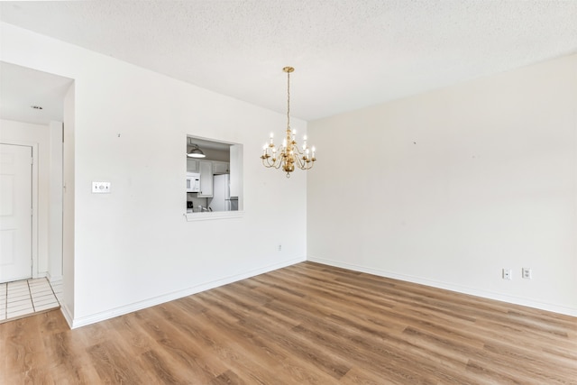 spare room featuring hardwood / wood-style floors, a textured ceiling, and an inviting chandelier