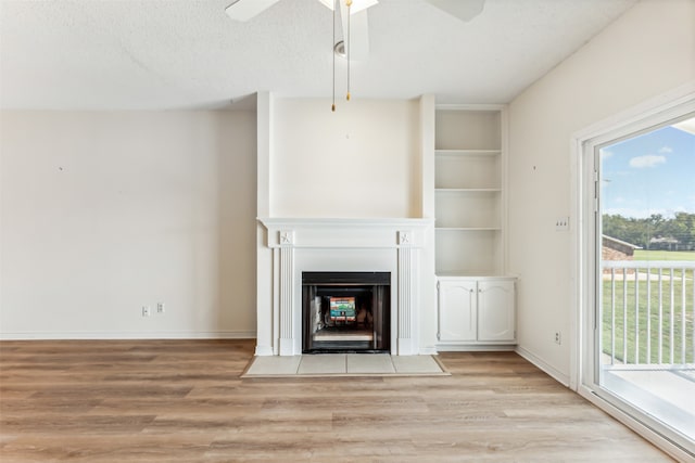 unfurnished living room featuring ceiling fan, built in shelves, light hardwood / wood-style floors, and a textured ceiling