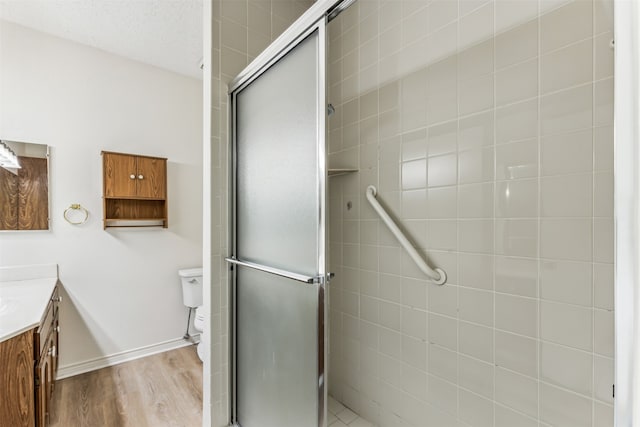 bathroom with toilet, a shower with shower door, a textured ceiling, vanity, and hardwood / wood-style floors