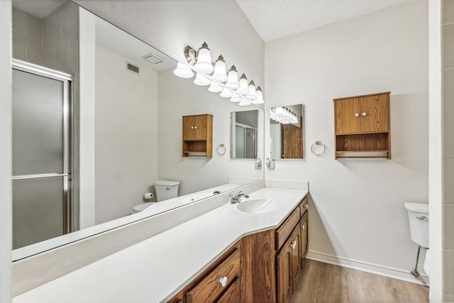 bathroom with wood-type flooring, vanity, walk in shower, toilet, and a textured ceiling