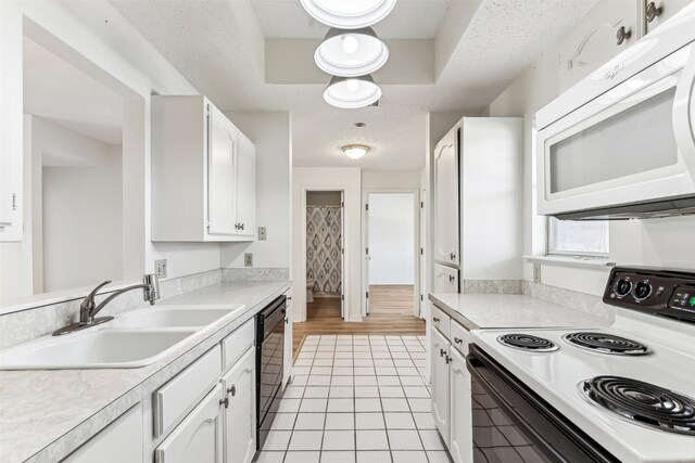 kitchen featuring white cabinetry, sink, light tile patterned floors, black appliances, and a raised ceiling